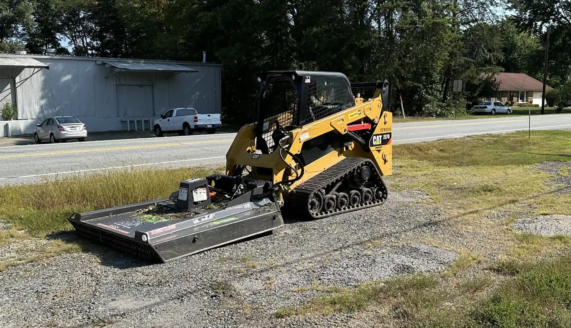 A yellow compact track loader with a brush cutter attachment photo